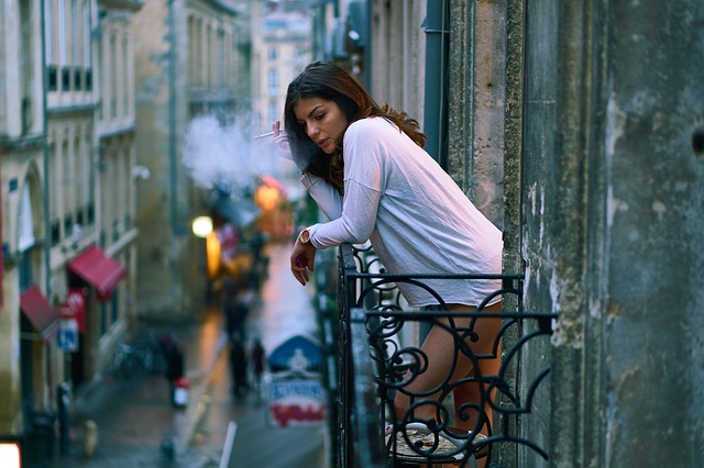 Žena v bielom tričku fajčí na balkóne a opiera sa o zábradlie